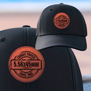 May include: Two black baseball caps with a brown leather patch that says "Combat Proven 5.56x45MM Since 1965".