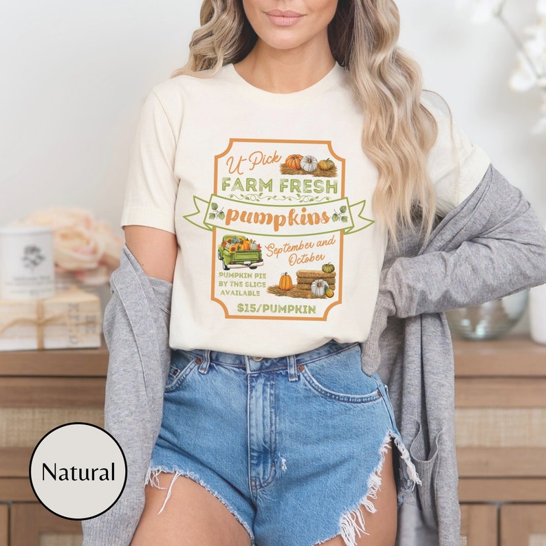May include: A white t-shirt with a graphic of a sign that says "U-Pick Farm Fresh Pumpkins" with a truck full of pumpkins and the text "September and October" and "Pumpkin Pie by the Slice Available $15/Pumpkin".