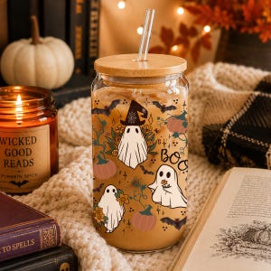 Peut inclure: Un verre transparent avec un couvercle en bambou et une paille en verre, rempli de caf&eacute; glac&eacute;. L'ext&eacute;rieur pr&eacute;sente un motif imprim&eacute; de fant&ocirc;mes blancs, de citrouilles orange, de chauves-souris noires et de fleurs, avec le mot BOO en noir.