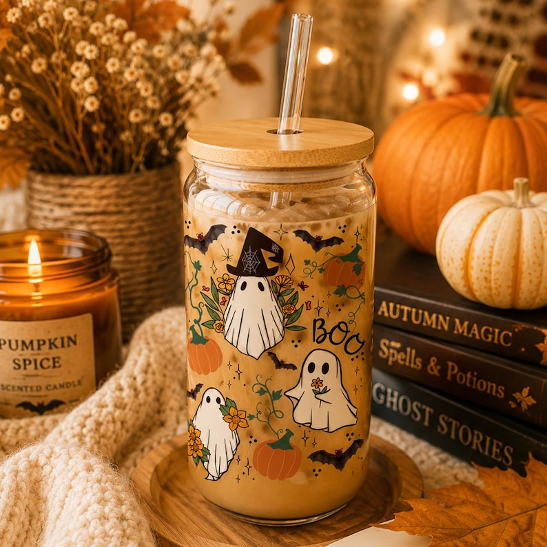 Peut inclure: Un verre transparent avec un couvercle en bambou et une paille en verre, rempli d'une boisson brun clair. Le verre pr&eacute;sente un motif imprim&eacute; de fant&ocirc;mes blancs, de citrouilles orange, de chauves-souris noires et de fleurs, avec le mot BOO.