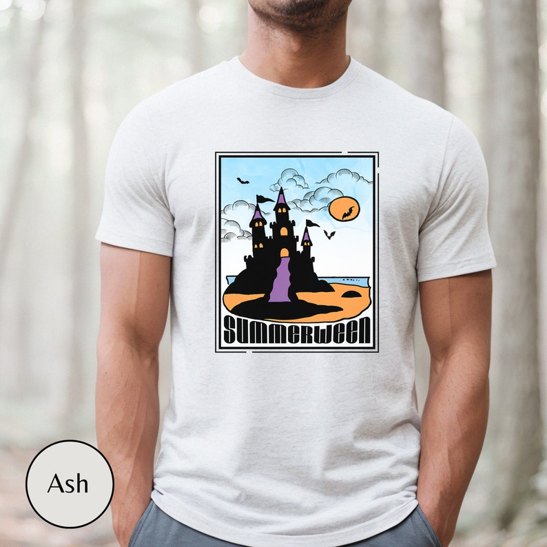 Pu&ograve; includere: Una maglietta bianca con una grafica di un castello nero su una spiaggia arancione con il testo "Summerween" in un font colorato.