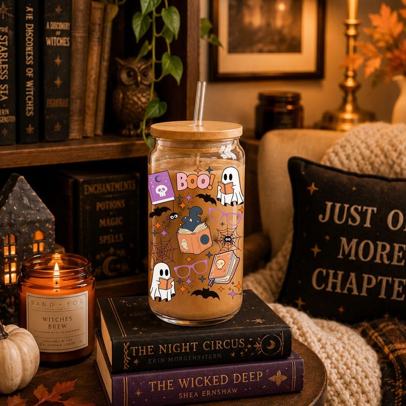 Puede incluir: Un vaso transparente con tapa de bamb&uacute; y pajita de cristal, lleno de una bebida de color marr&oacute;n claro. El exterior presenta calcoman&iacute;as coloridas con tem&aacute;tica de Halloween, incluyendo fantasmas, libros, ara&ntilde;as, telara&ntilde;as, murci&eacute;lagos y BOO.