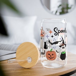 May include: A clear glass can with a spooky Halloween design. The can features ghosts, bats, a black cat, a pumpkin, and a cauldron. The text "Spooky" is written in a whimsical font on the can.