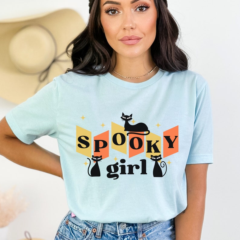 May include: A light blue t-shirt with a retro-style graphic featuring black cats and the text "spooky girl".