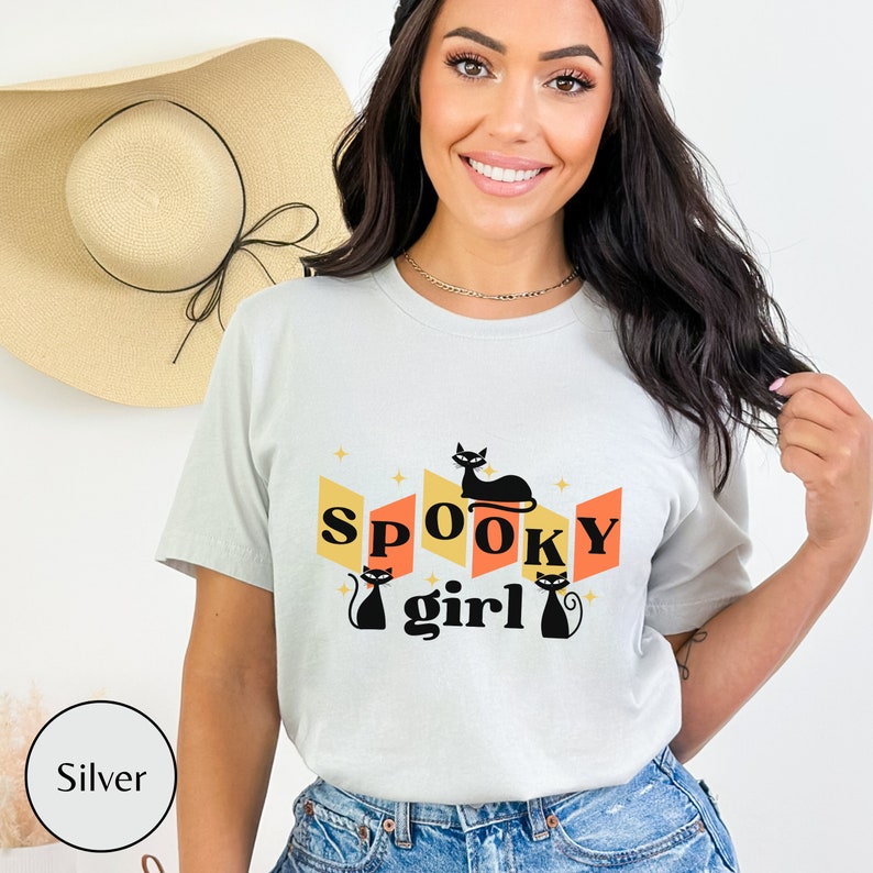 May include: A light gray t-shirt with a retro design featuring black cats and the text "SPOOKY girl".