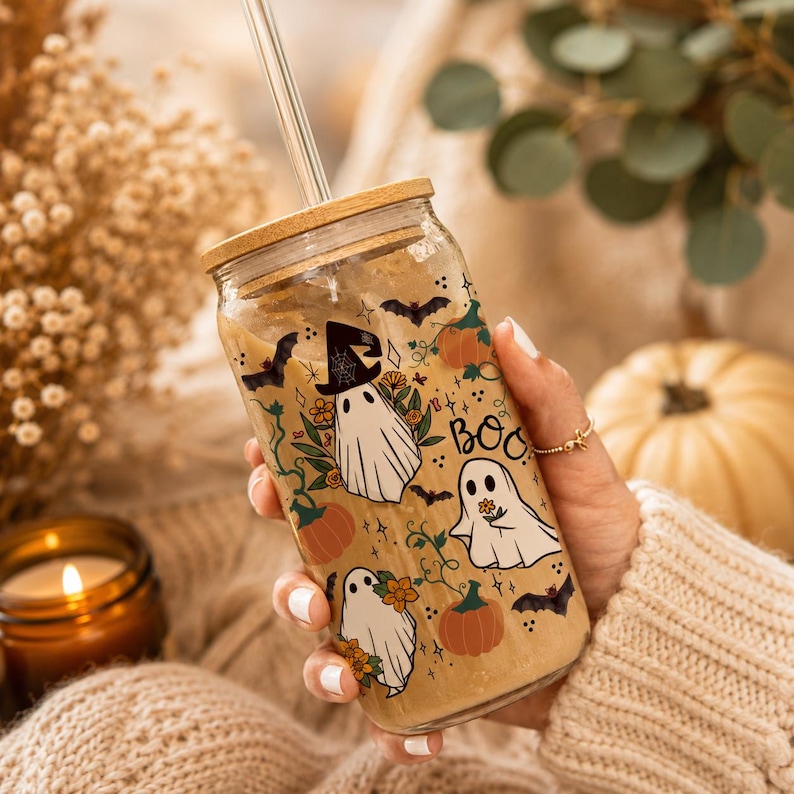 Peut inclure: Un verre transparent avec un couvercle en bambou et une paille en verre, rempli d'une boisson beige. L'ext&eacute;rieur pr&eacute;sente un motif imprim&eacute; de fant&ocirc;mes blancs, de citrouilles orange, de chauves-souris noires et de fleurs jaunes avec le mot BOO.