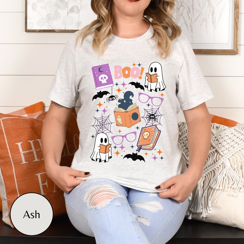 May include: A gray t-shirt with a Halloween-themed design featuring ghosts, bats, spiders, books, glasses, and the word "Boo!" printed on it.