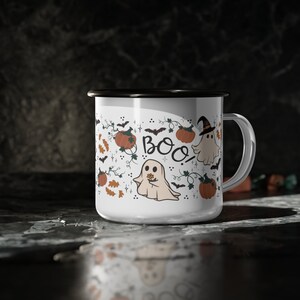 May include: White ceramic mug with a black rim and handle. The mug features a Halloween-themed design with ghosts, pumpkins, and the word "BOO!" in black lettering.