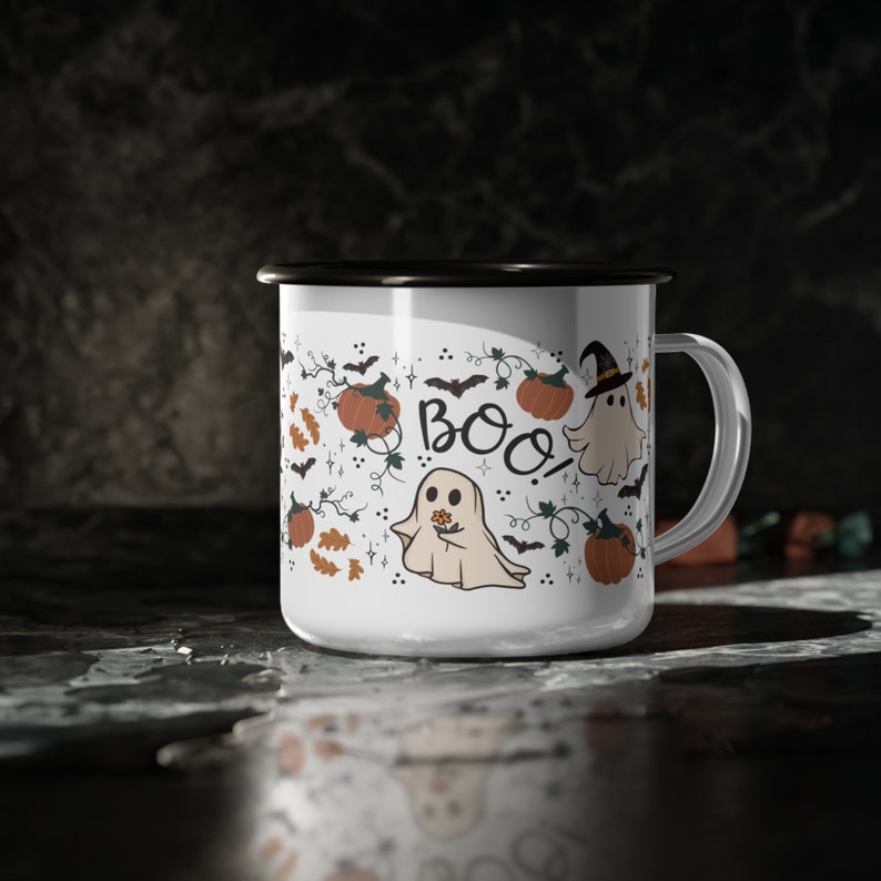 May include: White ceramic mug with a black rim and handle. The mug features a Halloween-themed design with ghosts, pumpkins, and the word "BOO!" in black lettering.