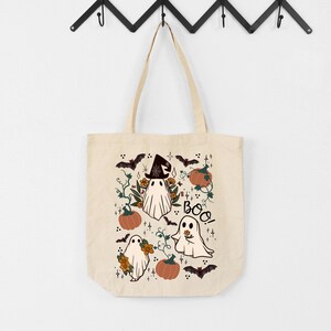 K&ouml;nnte beinhalten: Beige Tragetasche mit einem Halloween-Motiv. Das Design umfasst Cartoon-Geister, K&uuml;rbisse, Flederm&auml;use und florale Elemente. Das Wort "Boo!" ist in einer verspielten Schriftart geschrieben. Die Tasche hat eine einfache, rechteckige Form mit zwei Griffen.