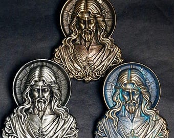 Op de afbeelding: Drie gedetailleerde metalen religieuze medaillons met een buste van Jezus met een halo. De medaillons zijn in brons-, zilver- en blauwtinten, elk met ingewikkelde details en een kruisontwerp.