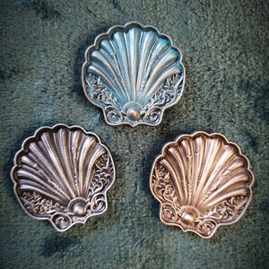 May include: Three decorative seashell-shaped trinket dishes. One is teal blue, and the other two are gold.