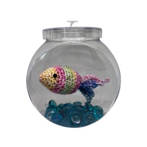 May include: A crocheted rainbow fish in a clear plastic jar with blue glass pebbles at the bottom.