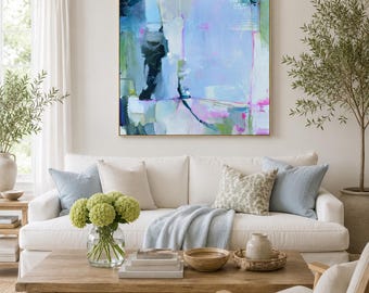 May include: A square abstract painting featuring a palette of light blue, white, green, and dark navy tones with thin magenta lines. The artwork is displayed in a thin wooden frame and hangs on a neutral wall above a white sofa with pillows.