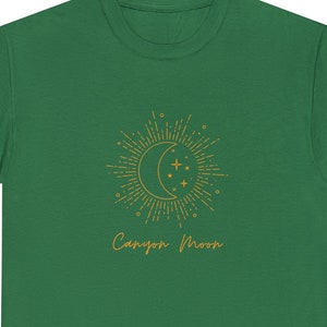 May include: A green t-shirt featuring a gold crescent moon and stars graphic with the text "Canyon Moon" printed on the front.
