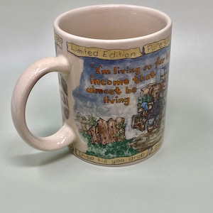 May include: A white ceramic mug with a brown, green, and blue illustration of a cartoon character carrying bags of shopping. The mug has the text "Limited Edition" and "Pure Silk" on the top and "I'm living so far on income that I almost be living" and "Shop till you drop" on the bottom.