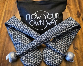 May include: A black zippered pouch with the text "FLOW YOUR OWN WAY" in white, accompanied by two navy and white chainmail-patterned items. Each item has a silver-colored ball with a white accent.