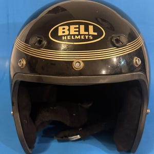 Pode incluir: Capacete de moto preto com detalhes dourados e o logotipo da Bell Helmets.