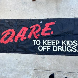 May include: A black banner with the word "DARE" in red letters and the text "TO KEEP KIDS OFF DRUGS." in white letters.