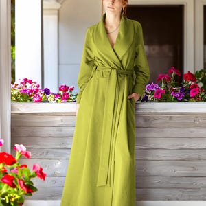 May include: A floor-length, chartreuse green robe featuring a wide shawl collar, long sleeves, and a matching fabric tie belt at the waist. The garment has a wrap-front design with a clean, solid-colored finish and visible side pockets.