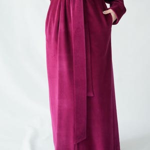 Pu&ograve; includere: Lungo accappatoio in velluto magenta con cintura abbinata. L'accappatoio ha maniche lunghe e tasche. La cintura &egrave; annodata in vita, stringendo l'accappatoio. Il tessuto ha un aspetto morbido e lussuoso.