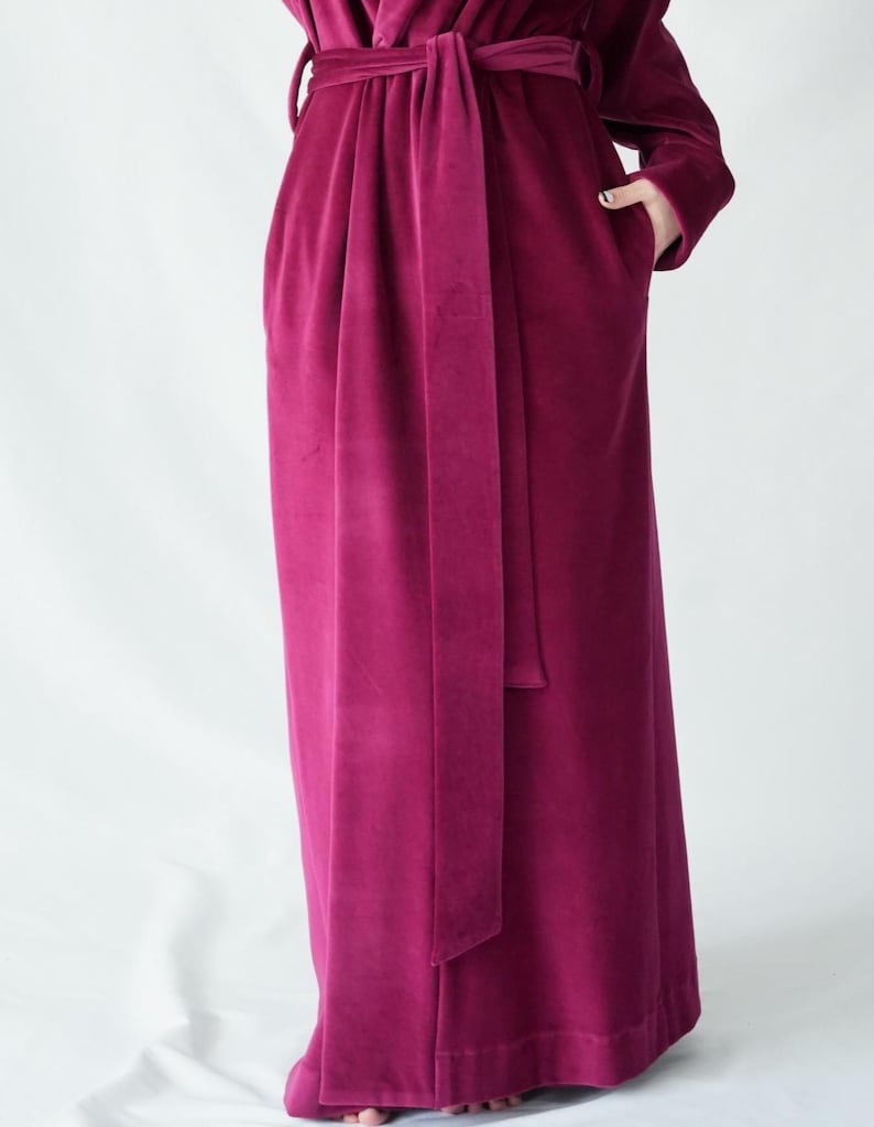 Pu&ograve; includere: Lungo accappatoio in velluto magenta con cintura abbinata. L'accappatoio ha maniche lunghe e tasche. La cintura &egrave; annodata in vita, stringendo l'accappatoio. Il tessuto ha un aspetto morbido e lussuoso.