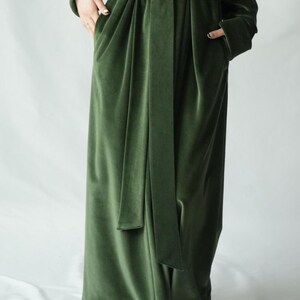 May include: A long, olive green velvet robe with a matching belt. The robe has long sleeves and pockets. The fabric has a soft, luxurious appearance. The robe is designed for comfort and style.