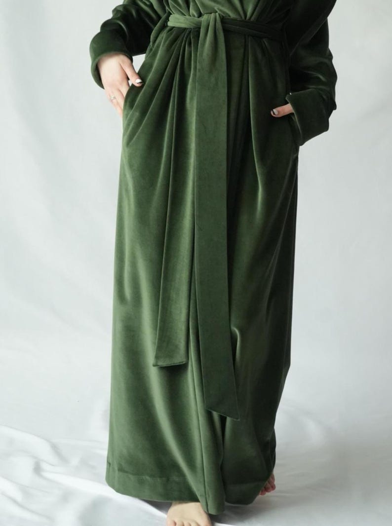 May include: A long, olive green velvet robe with a matching belt. The robe has long sleeves and pockets. The fabric has a soft, luxurious appearance. The robe is designed for comfort and style.