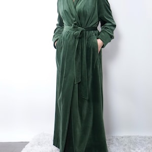 May include: A long, forest green velvet robe with a wrap-around design. The robe features a matching belt, long sleeves, and pockets. The soft, luxurious fabric drapes to the floor. The robe is a comfortable and elegant garment.
