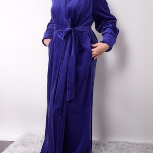May include: A long, royal blue velvet robe with a matching tie belt. The robe has long sleeves and pockets. The soft, plush fabric drapes to the floor. A comfortable and elegant loungewear option.