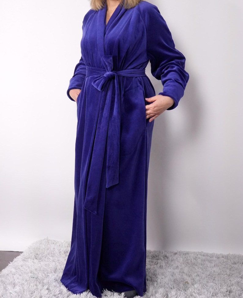 May include: A long, royal blue velvet robe with a matching tie belt. The robe has long sleeves and pockets. The soft, plush fabric drapes to the floor. A comfortable and elegant loungewear option.