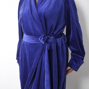 May include: A long, royal blue velvet robe with long sleeves and a wrap-around design. The robe features a matching belt tied at the waist. The soft, plush fabric drapes elegantly, creating a luxurious and comfortable garment. A classic piece for lounging.