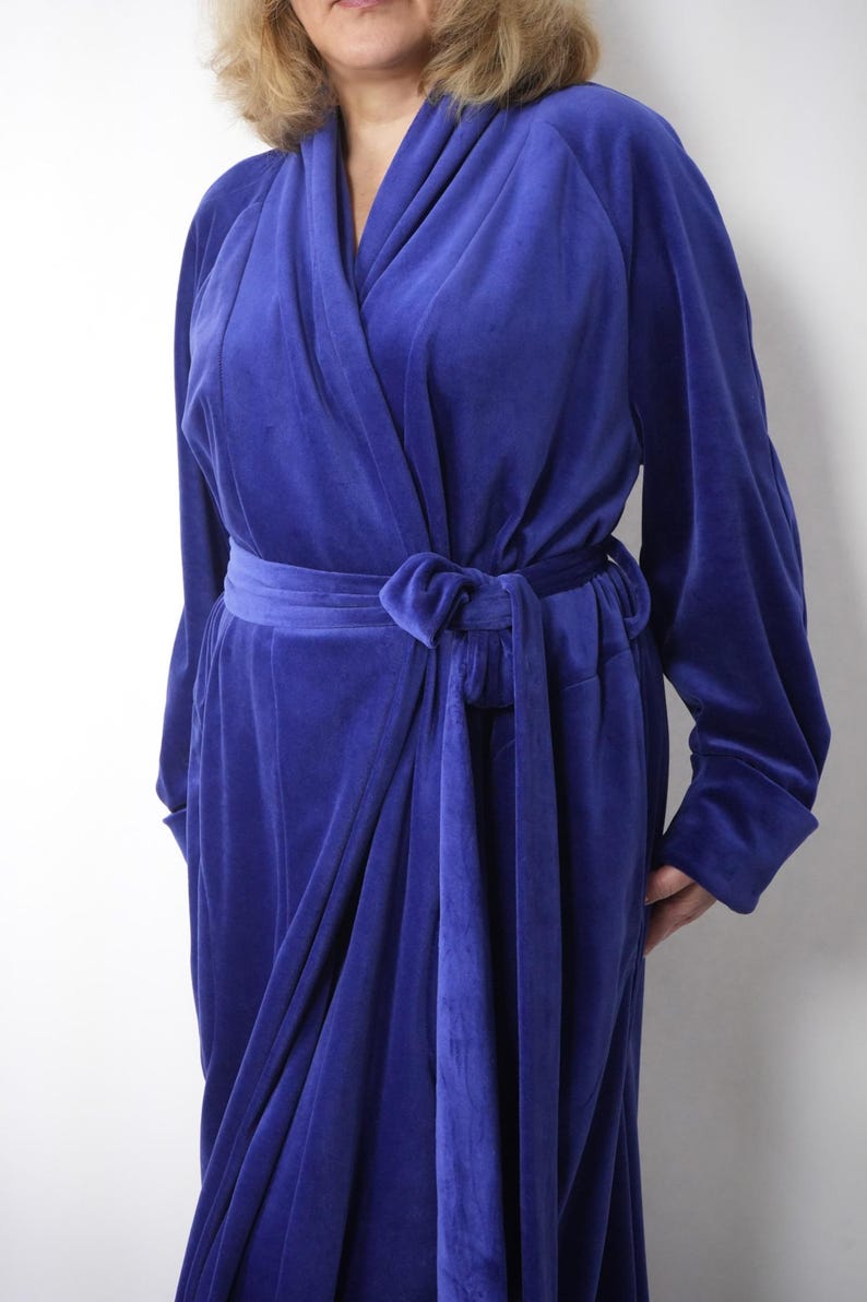 May include: A long, royal blue velvet robe with long sleeves and a wrap-around design. The robe features a matching belt tied at the waist. The soft, plush fabric drapes elegantly, creating a luxurious and comfortable garment. A classic piece for lounging.