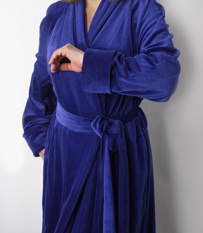 May include: A long, royal blue velvet robe with a wrap-around design and a matching belt tied at the waist. The robe features long sleeves and a shawl collar. The fabric appears soft and luxurious, suitable for lounging.