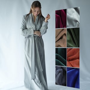 Pu&ograve; includere: Un lungo accappatoio grigio chiaro con cintura abbinata. L'accappatoio &egrave; realizzato in un materiale morbido e ha un collo a scialle. A destra, un'esposizione di campioni di tessuto di velluto in vari colori.