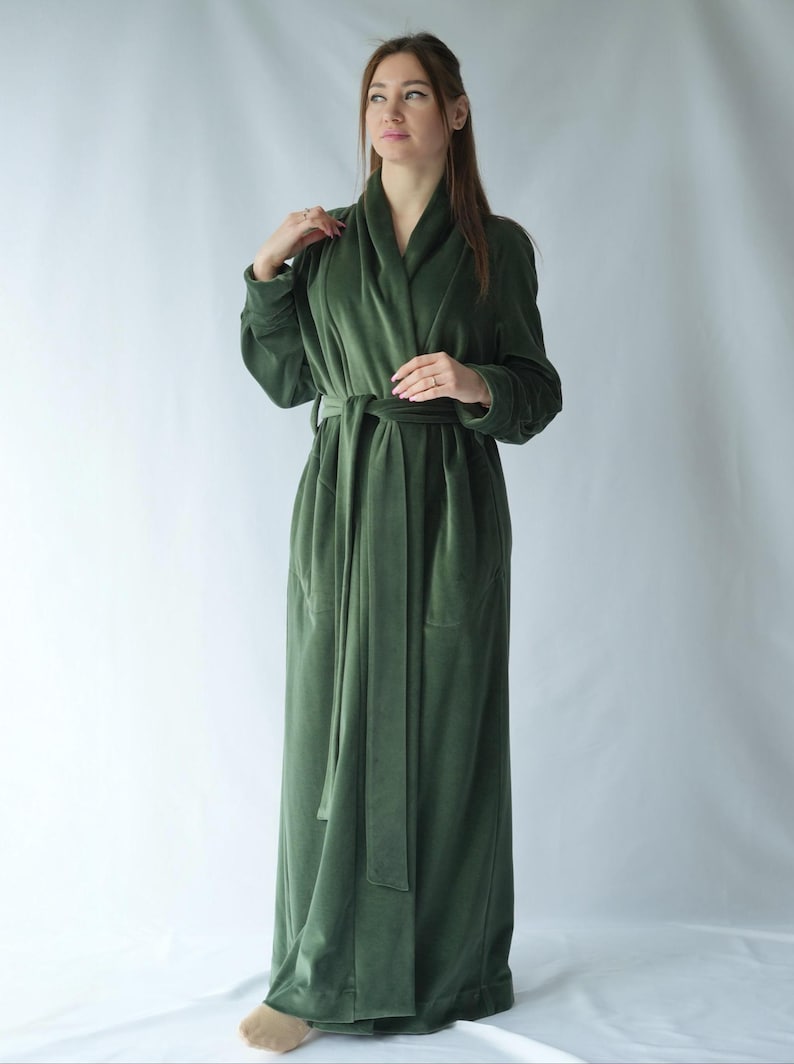 Pu&ograve; includere: Un lungo accappatoio verde oliva con collo a scialle e cintura abbinata. L'accappatoio &egrave; realizzato in un materiale morbido e vellutato e ha tasche. Le maniche sono lunghe e l'accappatoio arriva alle caviglie.