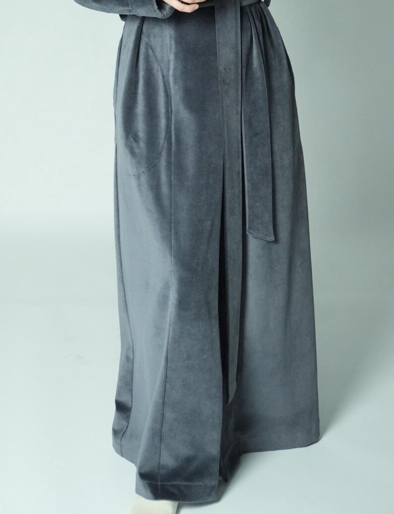 Pu&ograve; includere: Gonna lunga in velluto grigio con cintura abbinata. La gonna ha una vita alta e una leggera forma ad A. Il tessuto appare morbido e cade elegantemente. Lo stile generale &egrave; sofisticato e confortevole.