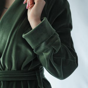 Pu&ograve; includere: Un accappatoio di velluto verde scuro con maniche larghe e una cintura abbinata. L'accappatoio ha un collo a scialle e un aspetto morbido e lussuoso. Il tessuto ha una lucentezza sottile, che suggerisce un materiale di alta qualit&agrave;. Lo stile generale &egrave; elegante e confortevole.