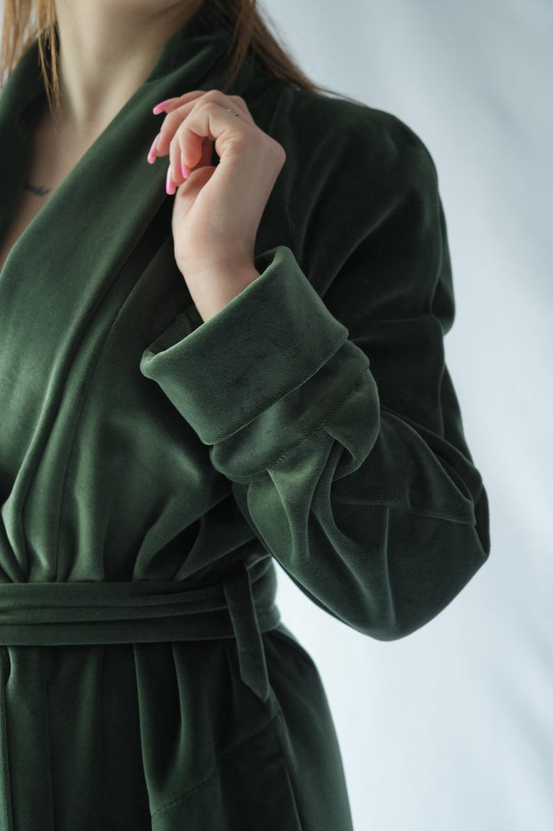 Pu&ograve; includere: Un accappatoio di velluto verde scuro con maniche larghe e una cintura abbinata. L'accappatoio ha un collo a scialle e un aspetto morbido e lussuoso. Il tessuto ha una lucentezza sottile, che suggerisce un materiale di alta qualit&agrave;. Lo stile generale &egrave; elegante e confortevole.