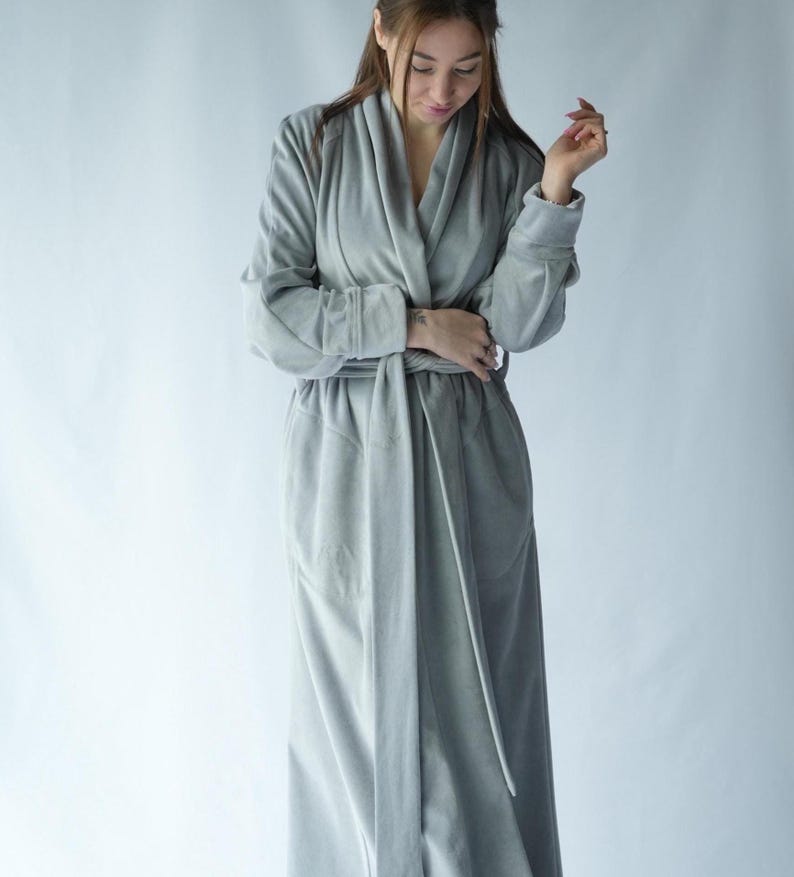 Pu&ograve; includere: Un lungo accappatoio grigio chiaro con collo a scialle e cintura abbinata. L'accappatoio &egrave; realizzato in un materiale morbido e felpato e ha maniche lunghe. L'accappatoio &egrave; progettato per il comfort e il relax.