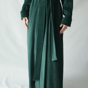 Pu&ograve; includere: Una lunga vestaglia di velluto verde smeraldo con cintura abbinata. La vestaglia ha maniche lunghe con polsini ripiegati. Il tessuto appare morbido e cade con eleganza. La vestaglia &egrave; legata in vita con una lunga cintura.