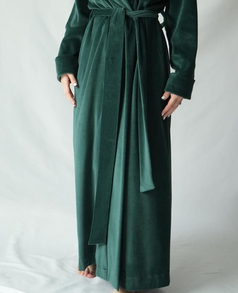 Pu&ograve; includere: Una lunga vestaglia di velluto verde smeraldo con cintura abbinata. La vestaglia ha maniche lunghe con polsini ripiegati. Il tessuto appare morbido e cade con eleganza. La vestaglia &egrave; legata in vita con una lunga cintura.