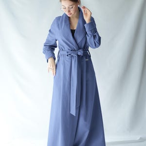 May include: A long, periwinkle-blue coat with a wrap-around design and a matching belt. The coat features a wide collar, long sleeves, and a floor-length hem. The belt is tied at the waist, and the coat is made of a soft, flowing fabric.