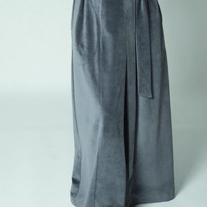 May include: A long, flowing, gray velvet robe with a matching belt. The robe has a soft, luxurious appearance and features a wrap-around design. The fabric drapes elegantly, suggesting comfort and style. The robe is suitable for lounging or as a stylish layering piece.