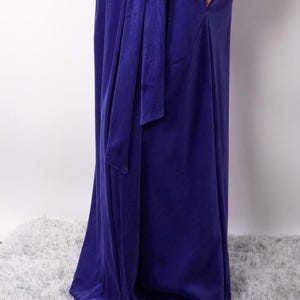 Pu&ograve; includere: Un lungo abito blu reale con una cintura in tessuto abbinata annodata in vita. L'abito presenta un design drappeggiato e una lucentezza sottile, che suggerisce un tessuto morbido e lussuoso. L'abito, lungo fino al pavimento, sembra essere realizzato in velluto o materiale simile.