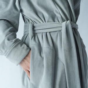 May include: A light gray robe with a wrap-around design and a matching belt tied at the waist. The robe has long sleeves and a pocket. The fabric appears soft and plush.