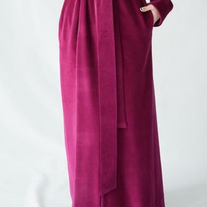 May include: A long, magenta velvet robe with a matching belt tied at the waist. The robe has long sleeves and pockets. The fabric has a soft, plush texture.