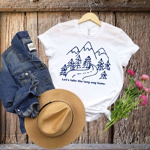 May include: White t-shirt with a blue mountain and road design. The text "Let's take the long way home." is printed below the design.