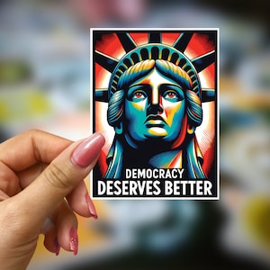 May include: A sticker featuring a colorful illustration of the Statue of Liberty with the text "Democracy Deserves Better".
