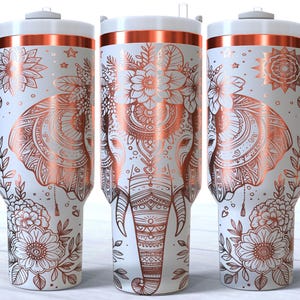 May include: Three white stainless steel travel mugs with a rose gold rim and handle. Each mug features a copper-coloured mandala design with an elephant and floral accents.